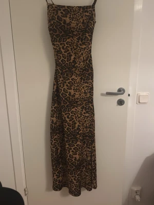 Leopardmönstrad långklänning - Säljer en snygg långklänning med leopardmönster och tunna axelband. Klänningen har en figurnära passform och är perfekt för dig som vill sticka ut. Materialet känns mjukt och följsamt, troligen polyester eller bomullsmix.