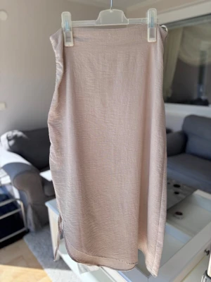 Beige/ljusrosa omlottkjol med snörning - Snygg beige/ljusrosa omlottkjol med snörning i sidan. Kjolen har en rak passform och är tillverkad i ett lätt, skrynkelfritt material som känns luftigt.