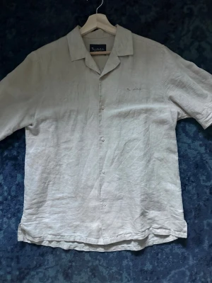 Beige linneskjorta från Bondelid - Säljer en stilren beige skjorta från Bondelid i svalt linne. Skjortan har korta ärmar, klassisk krage och knappar framtill. Perfekt för varma dagar och enkel att matcha med olika outfits. Diskret Bondelid-brodyr på bröstet.