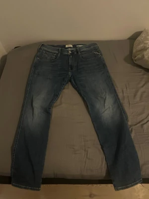 Blå raka jeans från replay Jeans - Säljer ett par klassiska blå jeans från report Jeans med rak passform och fem fickor. Jeansen har snygga slitningar och en tvättad look som ger en avslappnad vibe. Tillverkade i bomull för skön känsla och bra hållbarhet.