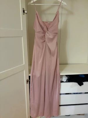 Ljusrosa långklänning från H&M - Säljer en elegant ljusrosa långklänning från bubbleroom med smala axelband och v-ringad omlottdesign framtill. Klänningen har en fin drapering vid bysten och är tillverkad i ett mjukt, glansigt material. Perfekt till balen! 