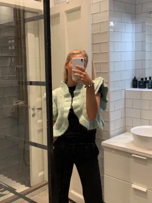 Mintgrön stickad bolero kofta med volanger - Supersöt stickad väst i mintgrönt med volangdetaljer längs ärmar och framkant. Kort modell som passar perfekt över en t-shirt eller klänning. Perfekt för att addera lite extra till din outfit.