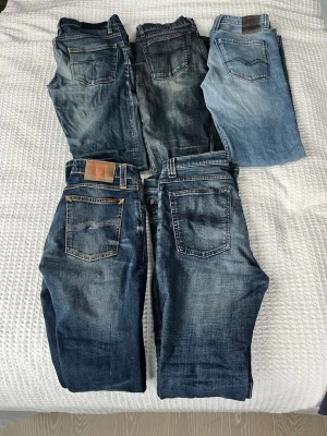 Fem par blå jeans från Nudie Jeans - Säljer fem par snygga blå jeans från Nudie Jeans i olika tvättar, från ljusblå till mörkblå. Klassisk femficksmodell med raka ben och tydliga slitningar för en avslappnad look. Perfekta för dig som gillar streetwear och tidlös denimstil.