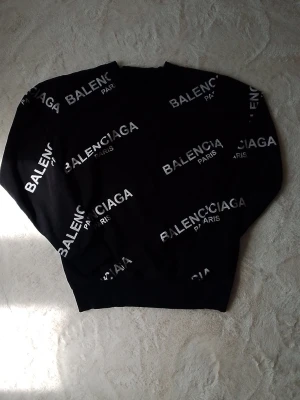 Svart Balenci sweatshirt passar size S/M - Cool svart sweatshirt från Balenci med vit logotyptext tryckt över hela tröjan. Klassisk rund halsringning och ribbade muddar vid ärmslut och nederkant. Perfekt för dig som gillar streetwear och vill sticka ut med ett trendigt plagg.