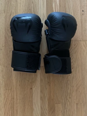 MMA handskar Venum - Säljer ett par svarta mma handskar från Venum med bred kardborrestängning för extra stöd runt handleden. Handskarna har en stilren design med Venum-logga och är tillverkade. Perfekta för träning och sparring inom kampsport. Storlek S så passar normal stora till mindre händer.