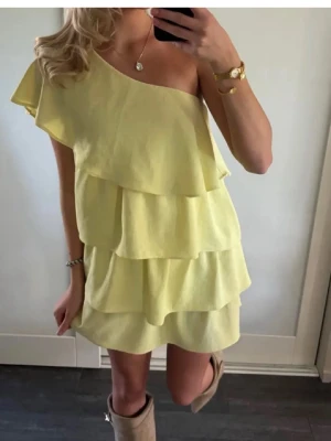 Gul oneshoulder volangklänning från zara - Superfin gul klänning med oneshoulder och flera volanglager. Perfekt för sommarens alla tillfällen, med en luftig och lekfull design. Klänningen är kort och har en snygg asymmetrisk axel. Materialet känns lätt och bekvämt.