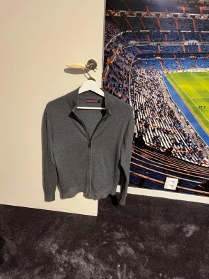 Mörkgrå ziptröja i cashmere -  Mörkgrå ziptröja med hög krage och dragkedja framtill. Tillverkad i en lyxig blandning av 40% cashmere, 45% viskos och 15% elastan för extra mjuk och stretchig känsla. Perfekt för dig som gillar stilrena och bekväma plagg.