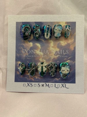 Blue/Green/HK (M);ExtraShortAlmond  - Unika handgjorda press-on naglar i blå och grön chrome med 3D dekorationer som stjärnor, kors, kedjor och Hello Kitty-detaljer. Naglarna har en extra kort, mandel form och coola silvriga inslag. Perfekt för dig som vill sticka ut med en kreativ och trendig nagelstil.M: 16 mm, 12 mm, 12,5 mm, 11,5 mm, 10 mm