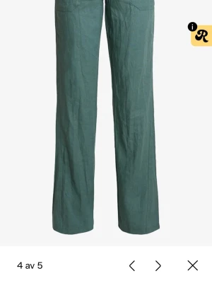 Gröna vida linnebyxor från Roxy  - Snygga gröna linnebyxor med avslappnad passform och raka, vida ben. Byxorna har dragsko i midjan med vita snören och stora fickor framtill. Perfekta för en chill och trendig look under varma dagar.