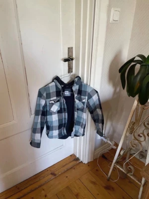 OBS!! Storleken är inte rätt i ”storlek” utan läs beskrivningen om du är intresserad!! Rutig jacka i blå och vit med huva - Snygg rutig jacka i blått, vitt och svart med dragkedja och två bröstfickor. I STORLEK  128🥰!! (Storlek 128 fanns inte i ”storlek” så jag behövde ta S som storlek)