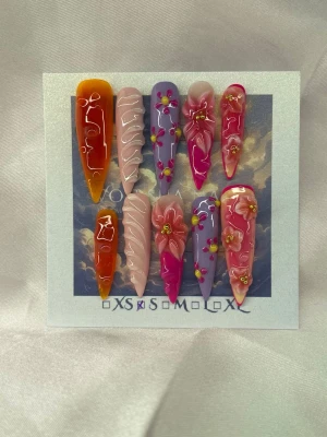 SummerDreams (S);Extra Long Stiletto - Säljer ett set handgjorda press-on naglar i en extra lång stilettoform med mixade färger som orange, lila, rosa och nude. Naglarna har 3D-blommor, guldpärlor och vita swirl-detaljer för en unik och kreativ look. S: 15 mm, 11,5 mm, 12 mm, 11 mm, 9 mm , med glansig finish och dekorationerna ger en extra wow-effekt.