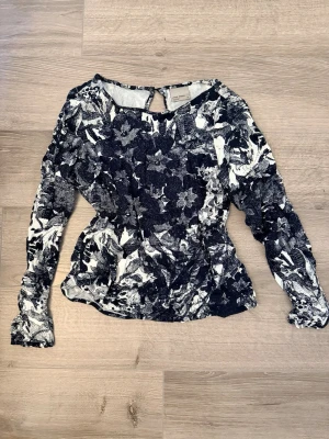 Långärmad blus Vero Moda XS - Snygg blus från Vero Moda i storlek XS med svartvitt blommönster. Blusen har långa ärmar, figurnära passform och en liten knapp i nacken. Materialet känns mjukt och lätt. 