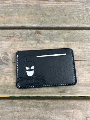 Svart Batman kortfodral i läder - Snyggt svart kortfodral i läder med Batman-motiv präglat på framsidan. Kortfodralet har vita sömmar runt kanterna och plats för flera kort. Perfekt för dig som gillar superhjältar och vill ha något unikt i fickan.