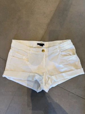 Vita shorts som är uppvikta nedtill  - Snygga vita shorts med low/ midwaist passform och uppvikta vid benslut. Klassisk femficksmodell med knapp och dragkedja framtill. Perfekta för varma dagar och enkla att matcha med olika toppar. Lite slitage på knappen som man kan se på bilden, men syns inte från lite avstånd.