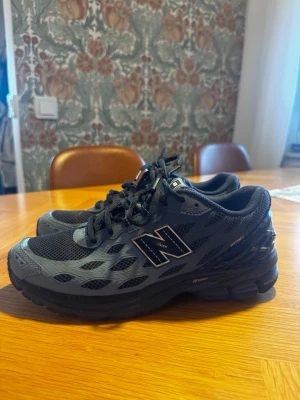 Svarta New Balance sneakers - Snygga svarta sneakers från New Balance med mesh- och syntetmaterial. Skorna har en sportig design med reflekterande detaljer och den klassiska N-loggan på sidan. Perfekta för dig som gillar streetwear och vill ha bekväma skor till vardags.