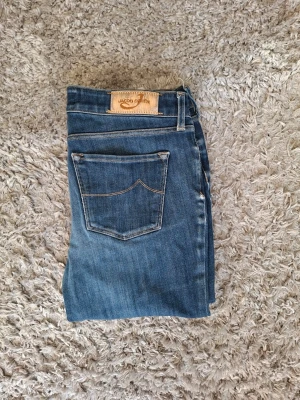 Blå raka jeans från Jacob Cohen - Snygga blå jeans från Jacob Cohen med klassisk femficksdesign och raka ben. Jeansen har en läderpatch med logga bak och subtila slitningar framtill. Perfekta för en avslappnad och trendig look. Jeansen har några defekter se bild
