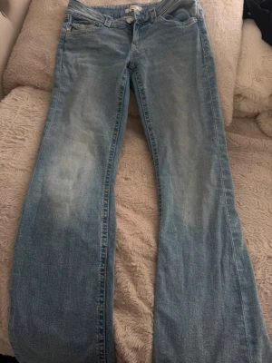 Ljusblå bootcut jeans - Säljer ett par ljusblå bootcut jeans med klassisk femficksdesign och dragkedja fram. Jeansen har en lätt tvättad look och är tillverkade i denim med lite stretch för skön passform. Perfekta till en avslappnad stil.