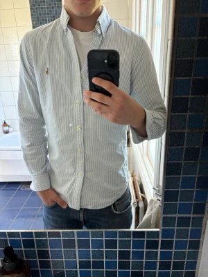 Randig skjorta från Polo Ralph Lauren - Säljer en klassisk ljusblå och vit randig skjorta från Polo Ralph Lauren. Skjortan har button-down krage, långa ärmar och små broderade logotypdetaljer på bröstet. Ta kontakt vid intresse 😊