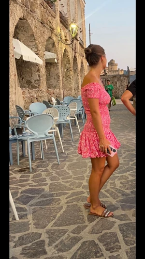 Rosa smockad klänning - Supersöt rosa kortklänning med offshoulder och volangkant. Klänningen har ett smockat liv och ett vitt mönster över hela tyget. Perfekt för varma dagar och ger en riktigt somrig vibe.