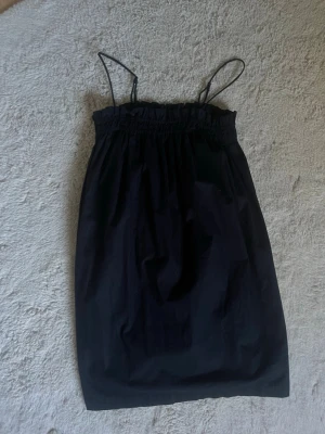 Svart axelbandslös klänning - Säljer en svart klänning med resår upptill och rak passform. Klänningen är kort och har tunna axelband som kan bäras eller stoppas in för en bandeau-look. Perfekt för sommardagar eller när du vill ha något enkelt och stilrent.