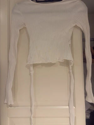 Vit rosett tröja💕 - Superfin, vit ribbad långärmad tröja från FB Sister med en riktigt snygg detalj i ryggen! Den är öppen baktill och har långa band som man knyter till en söt rosett. Perfekt croppad modell som passar till allt!