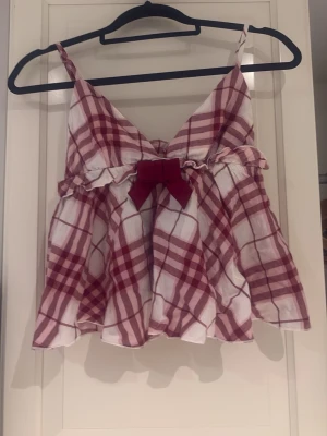 Randigt nattlinne 💕 - Superfin rutig babydoll-top från Gina Tricot med smala axelband, söt volang och en röd rosett framtill. Otroligt fin passform som är lite utställd nedtill (peplum-stil). Perfekt för en trendig Y2K- eller Coquette-look!