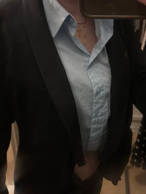 Svart kavaj med volangkant - Stilren svart kavaj med volangkant framtill och smal passform. Kavajen har långa ärmar, två fickor och ett randigt innerfoder. Perfekt för dig som vill ha en trendig och elegant look.