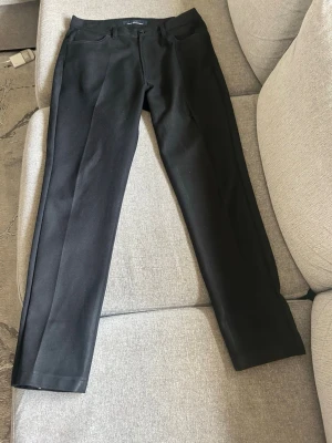 Svarta kostymbyxor från Jeff Company - Snygga svarta kostymbyxor från Jeff Company med klassisk rak passform och hällor för bälte. Byxorna har diskreta fickor och stängs med knapp och dragkedja. Perfekta för en stilren look.