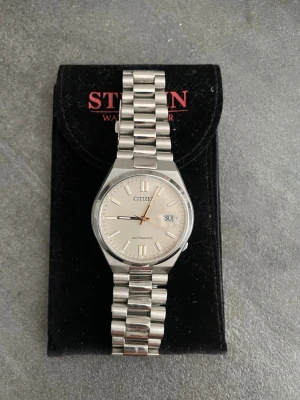 Citizen Tsuyosa - Stilren automatisk klocka från Citizen i silverfärgat stål med klassisk länkarmband och ljus urtavla. Klockan har datumvisning och levereras med extra länkar. Perfekt accessoar för dig som gillar tidlös design.