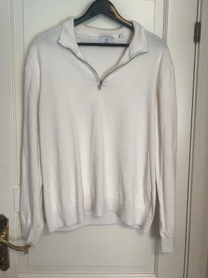 Vit halvzip tröja med krage - Vit långärmad tröja med halvzip och krage. Tröjan har ribbade muddar vid ärmslut och nederkant, samt en stilren och enkel design. Perfekt för lager-på-lager och passar till många olika outfits.
