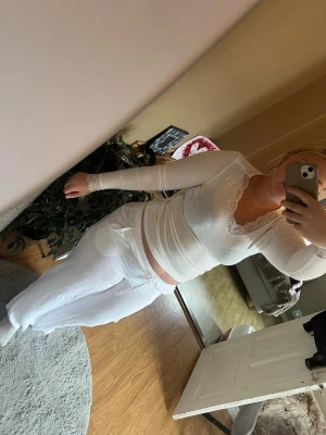 Vitt loungewear-set med spetsdetaljer - Säljer ett vitt loungewear-set med långärmad topp och byxor. Toppen har v-ringning och spetsdetaljer vid halsringning och ärmslut. Byxorna har resår och dragsko i midjan för skön passform. Perfekt för mysiga hemmakvällar.