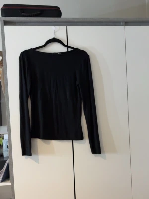 Svart långärmad topp från 157 - En enkel och stilren svart långärmad topp från 157. Modellen har en rund halsringning och är tillverkad i ett mjukt material som sitter skönt mot kroppen. Perfekt att matcha med jeans eller kjol för en clean look.
