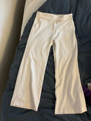 Vita kostymbyxor från H&M -  vita kostymbyxor från H&M med raka ben och diskreta fickor i sidorna. Byxorna har en klassisk passform och stängs med hake och dragkedja. 
