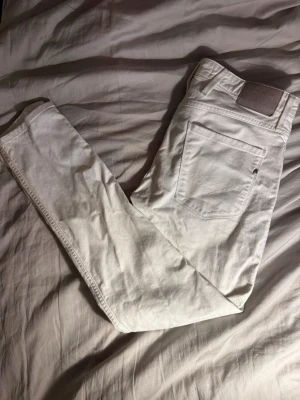 REPLAY  - Säljer ett par vita jeans med raka ben och klassiska bakfickor. Jeansen har bälteshällor och en patch vid linningen. Materialet är kraftigt bomullstyg som ger en clean och fräsch look.
