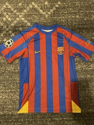 Barcelona matchtröja blå/röd  - Säljer en officiell FC Barcelona matchtröja från Dri-fit i blått och rött med gula detaljer. Tröjan har klubbmärke på bröstet, Champions League-märke på ärmen och är tillverkad i ett lätt, snabbtorkande material. Perfekt för fotbollsträning eller att bära till vardags.Bra skick. Storlek 176