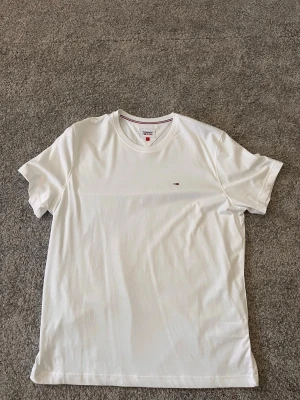 Vit t-shirt från Tommy Hilfiger - Klassisk vit t-shirt från Tommy Hilfiger med liten broderad logga på bröstet. T-shirten har rund halsringning och korta ärmar. Perfekt basplagg i mjuk bomull som passar till allt. XL men passar på M-L eftersom tvättning.
