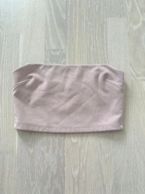 Ljusrosa bandeau tubtopp - Säljer en ljusrosa bandeau tubtopp. Toppen är axelbandslös och har en mjuk, stretchig passform som sitter skönt mot kroppen. Perfekt att matcha med jeans eller kjol. Toppen är mer rosa i verkligheten men det gick ej att få med pga ljuset😇