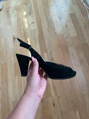 Svarta klackar - Säljer ett par svarta klackar med öppen tå och mellanbrded klack. Skorna har en justerbar rem runt hälen.
