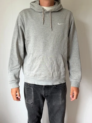 Grå hoodie från Nike med huva - Säljer en stilren grå hoodie från Nike med klassisk huva och dragsnören. Hoodien har en stor magficka och Nike-logga broderad på bröstet. Tillverkad i mjukt sweatshirtmaterial som är perfekt för chill dagar. Passar till det mesta och är superbekväm.