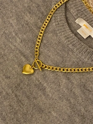Guldigt halsband med hjärthänge - Snyggt halsband i guldfärgad rostfritt stål med en chunky kedja och ett hjärtformat hänge. Halsbandet har en toggle-låsning som ger en trendig touch. Perfekt accessoar för att lyfta vilken outfit som helst.
