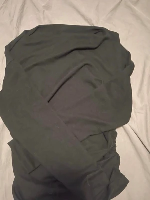 Svart långärmad topp med rynk - Snygg svart långärmad topp med rynkade detaljer på sidan som ger en cool och trendig look. Perfekt att styla med jeans eller kjol för en enkel men chic outfit. Tillverkad i mjukt material som känns skönt mot huden.