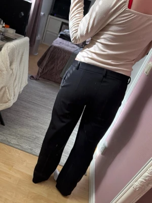 Svarta kostymbyxor med raka ben - Snygga svarta kostymbyxor med raka ben. Byxorna har bälteshällor, sidofickor och stängs med dragkedja och knapp. Perfekta för en clean och stilren look. Materialet är mjukt och har en lätt stretch för extra komfort.