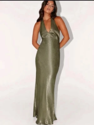 Bal klänning  - Stilren långklänning i glansigt grönt satinmaterial med djup v-ringning och smala axelband. Klänningen har en figurnära passform och faller snyggt längs kroppen. Perfekt för dig som vill ha en elegant look.