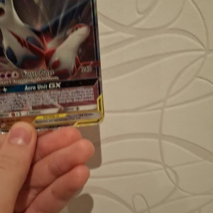 Pokémonkort Latias & Latios GX - Säljer ett Pokémonkort med Latias & Latios GX Tag Team. Kortet har en färgstark design med Latias och Latios i vitt, rött och blått mot en mörk bakgrund. Det är tillverkat i glansig kartong och har HP 250 samt attacker som Buster Purge och Aero Unit GX.