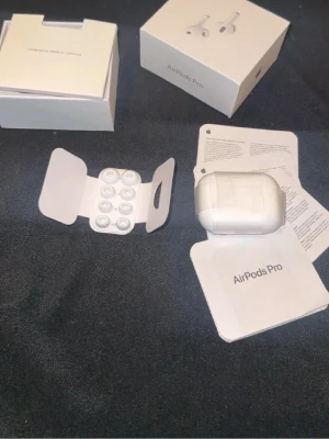 Apple AirPods Pro trådlösa hörlurar - Säljer ett par vita Apple AirPods Pro med laddningsetui. De är in-ear hörlurar med silikontoppar och har en stilren, kompakt design. Kommer med originalförpackning och manualer. 