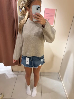 Blå jeanskjol med fransad kant - Säljer en kort blå jeanskjol med rå, fransad nederkant och slitna detaljer. Kjolen har klassisk femficksdesign och dragkedja fram. Perfekt för dig som gillar en avslappnad och trendig stil.