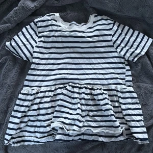 Randig topp från Zara med volang - Säljer en vit och marinblå randig topp från Zara med volang nedtill. Toppen har korta ärmar och en avslappnad passform. Perfekt för dig som gillar en enkel men ändå söt stil.