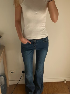 Blå bootcut jeans med låg midja - Säljer ett par klassiska blå bootcut jeans med låg midja och fem fickor. Jeansen har en snygg tvätt och är tillverkade i ett mjukt denimtyg med lite stretch för skön passform. Perfekta till en avslappnad stil och passar till det mesta.