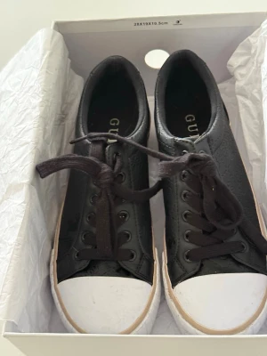 Svarta GUESS sneakers med logo mönster - Snygga och bekväma sneakers från GUESS i svart med diskret logomönster. Klassisk modell som passar till det mesta – både vardag och lite mer uppklätt. Använda men i fint skick (normalt slitage, se bilder).  Perfekta vardagsskor eller till fest. 