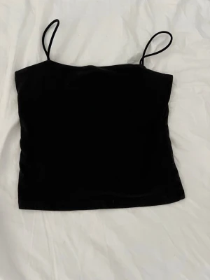 Svart sammetslinnetopp med smala band - Snygg kort svart linnetopp i mjuk sammet med tjocka axelband. Enkel och stilren design som passar perfekt till många olika looks. Toppen har en croppad passform och är ärmlös för en trendig vibe.